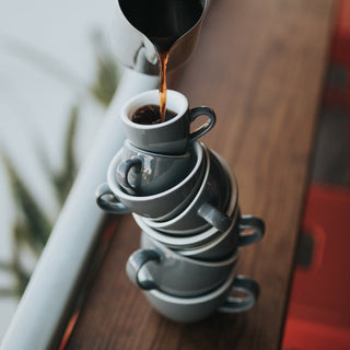 Coffee being poured into stack of coffee cups